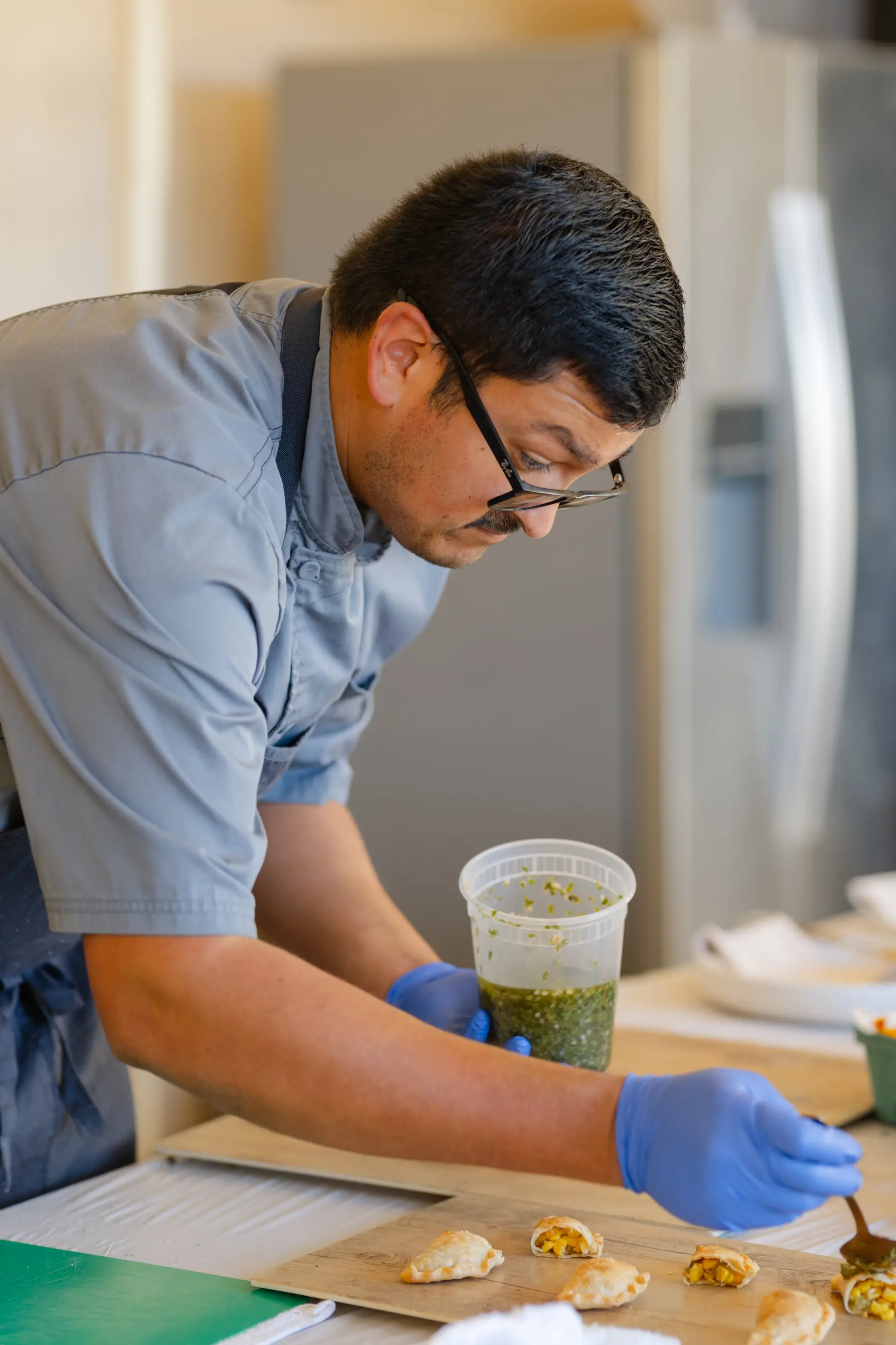 A chef spooning chimichurri over empanadas on a board at the prep table