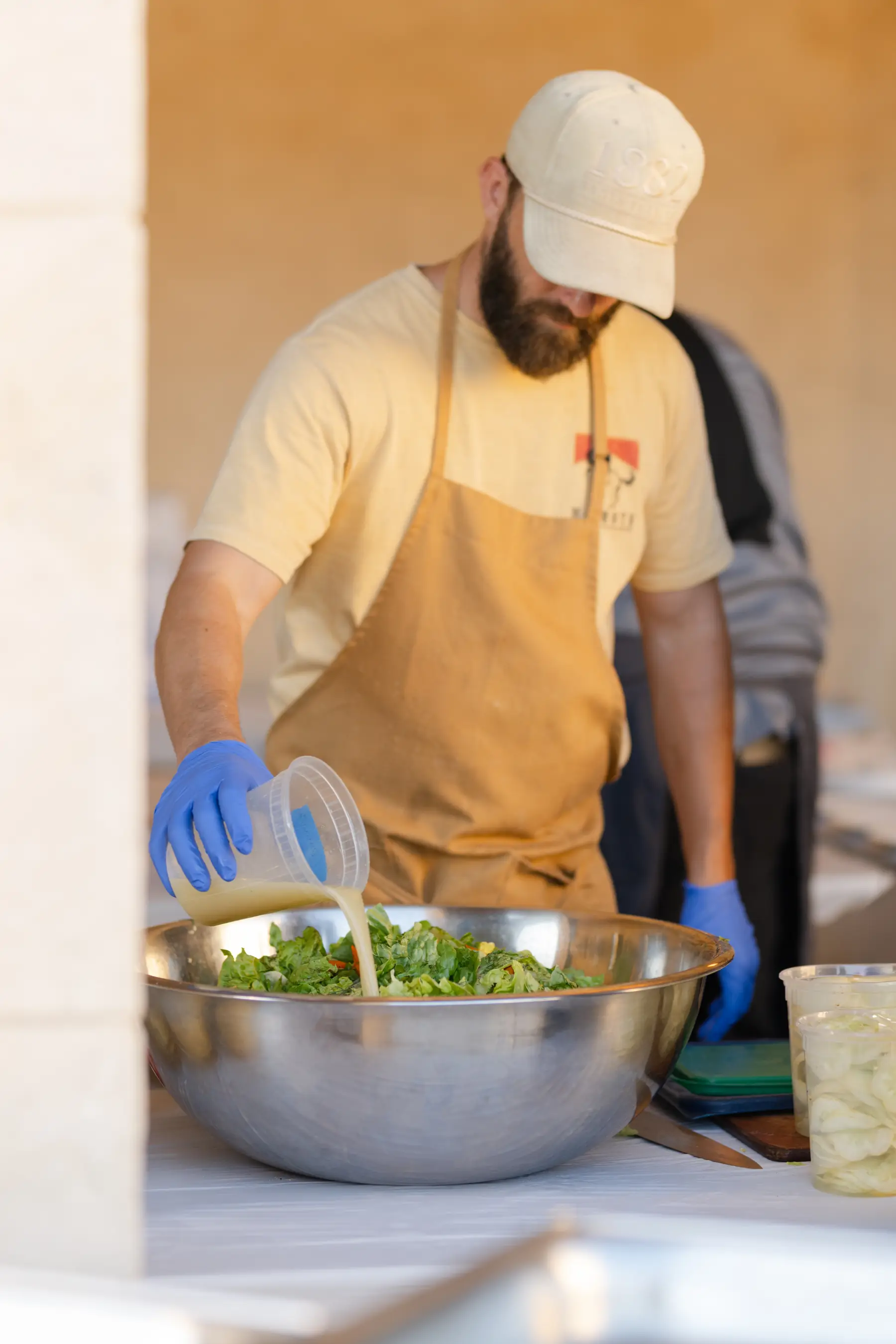 A chef pouring dressing over farm greens in a mixing bowl at the catering line