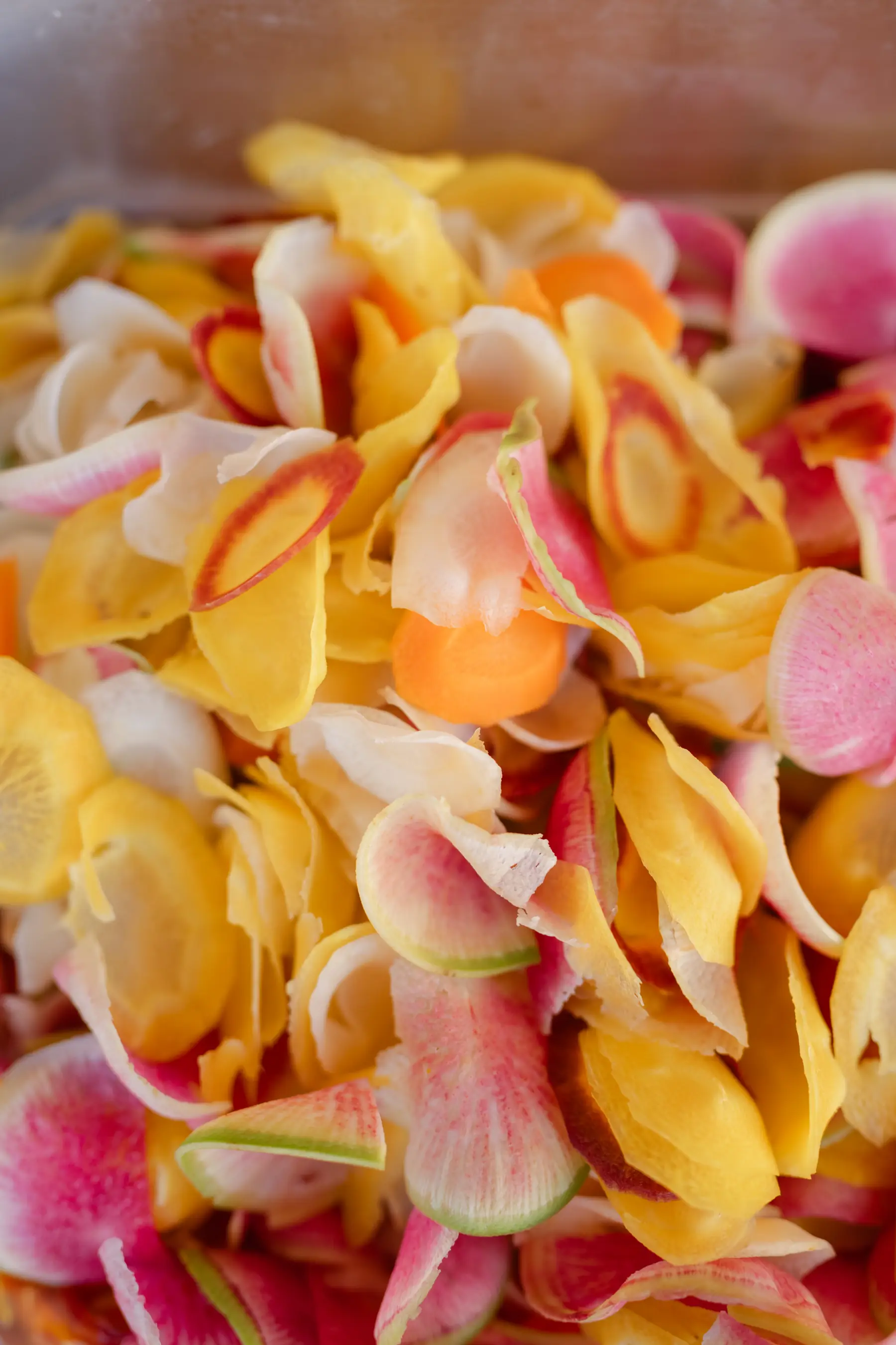 A tray of shaved watermelon radish, carrot and yellow root vegetables prepped for plating