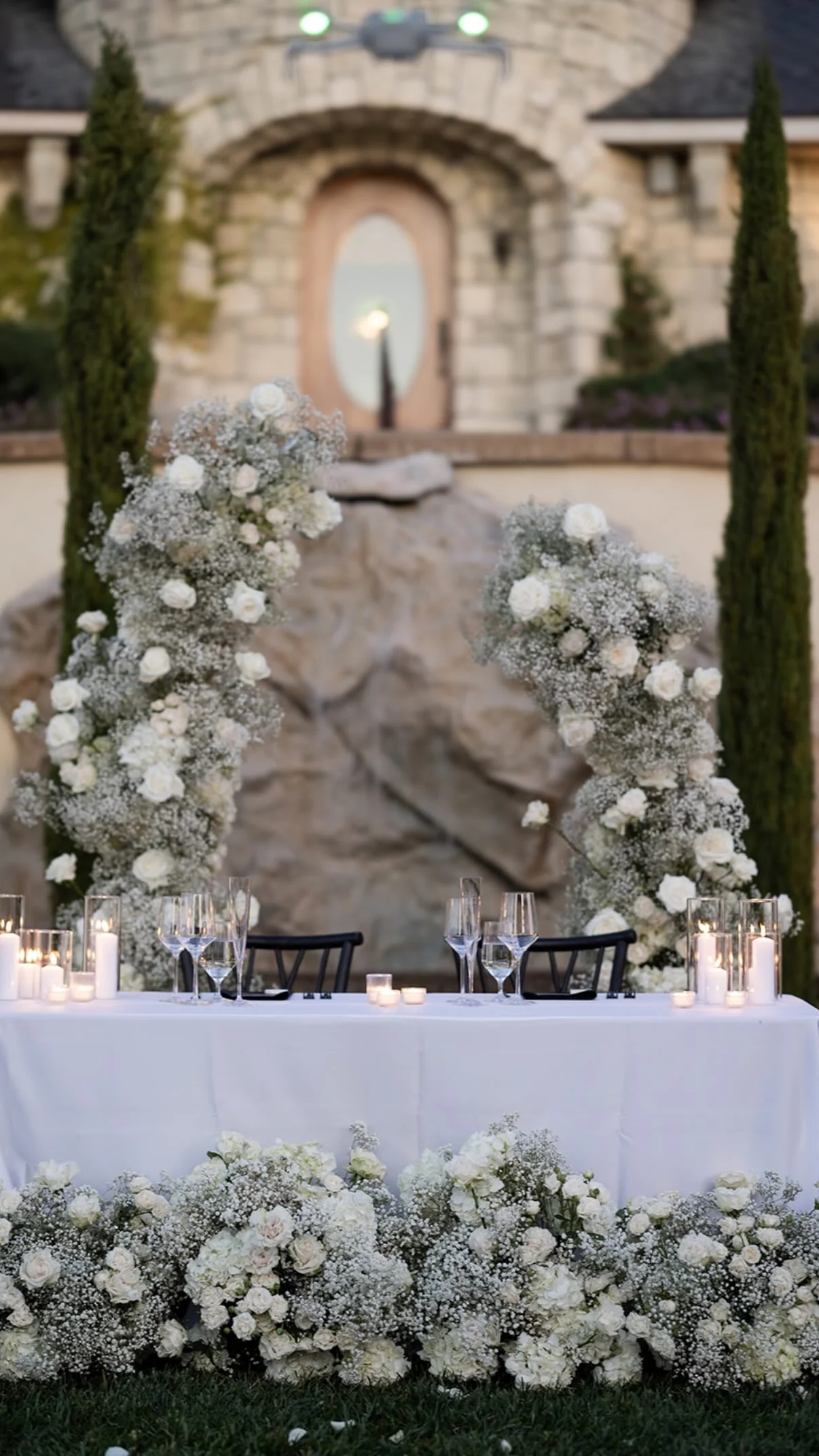 A candlelit table for two set before a white floral arch at Chateau Noland