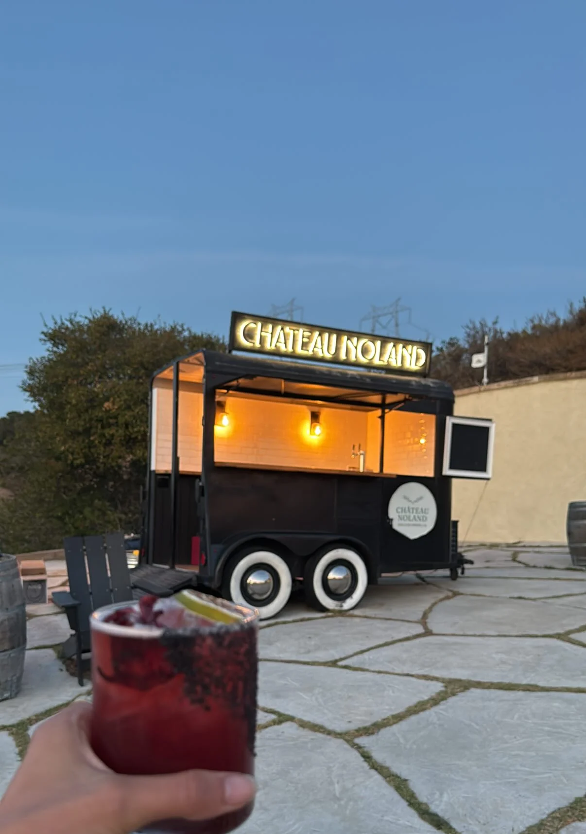 A cocktail held in front of the lit bar trailer at Chateau Noland