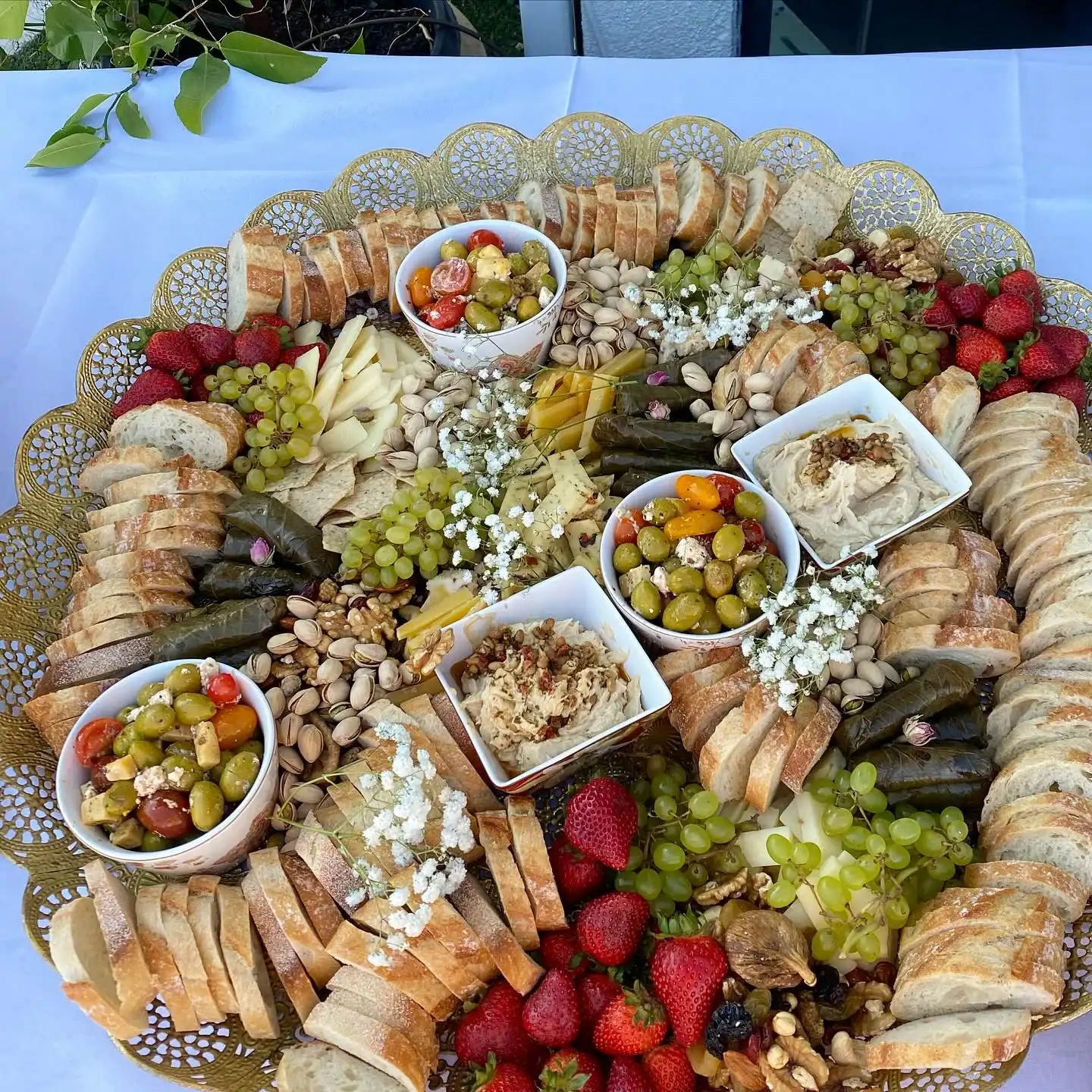 A grazing platter of sliced breads, cheeses, grapes, olives and dips on a gold tray
