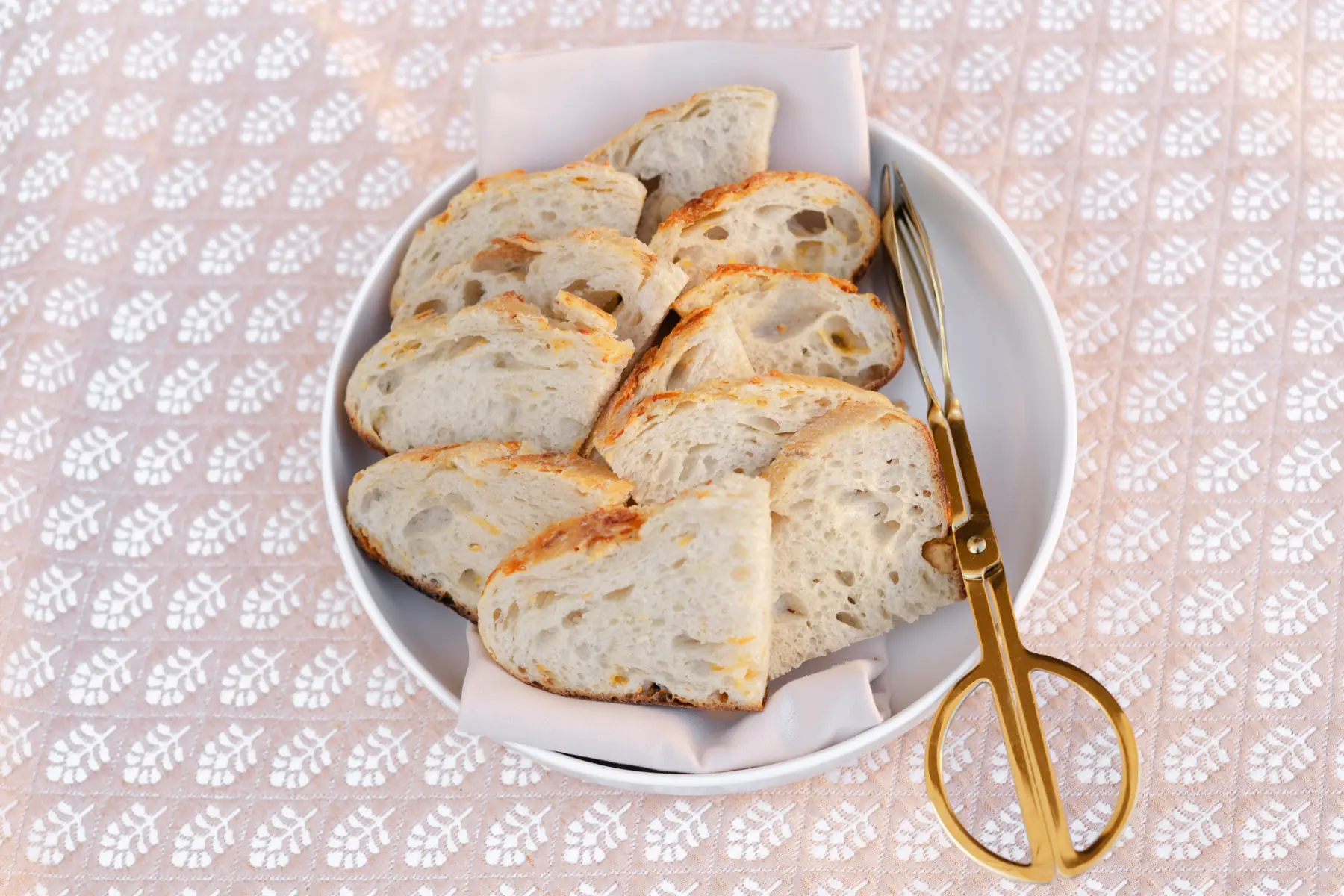 Sliced bread in a linen-lined bowl with gold serving tongs