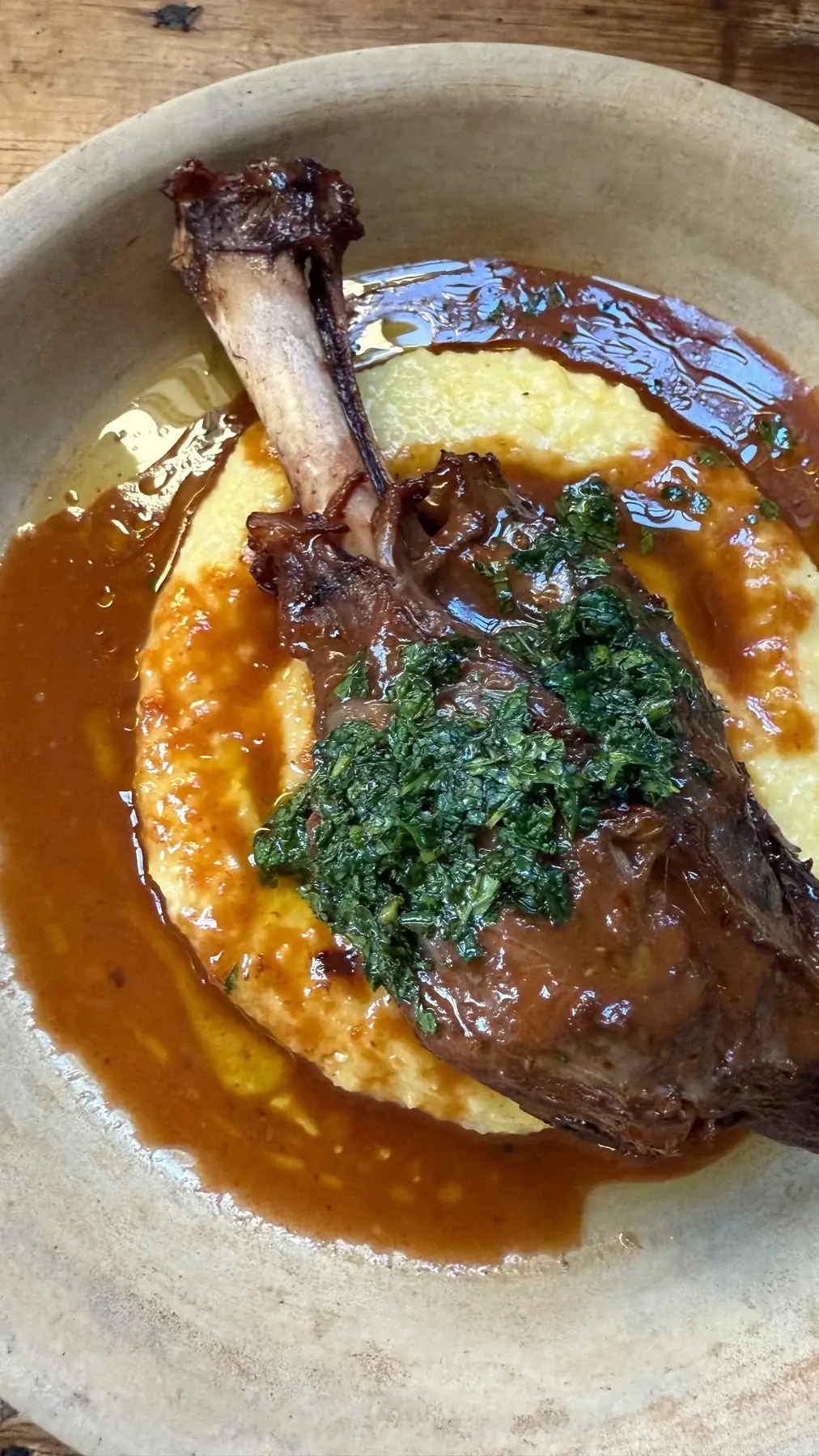 A braised lamb shank over polenta in a pan sauce, finished with herb salsa