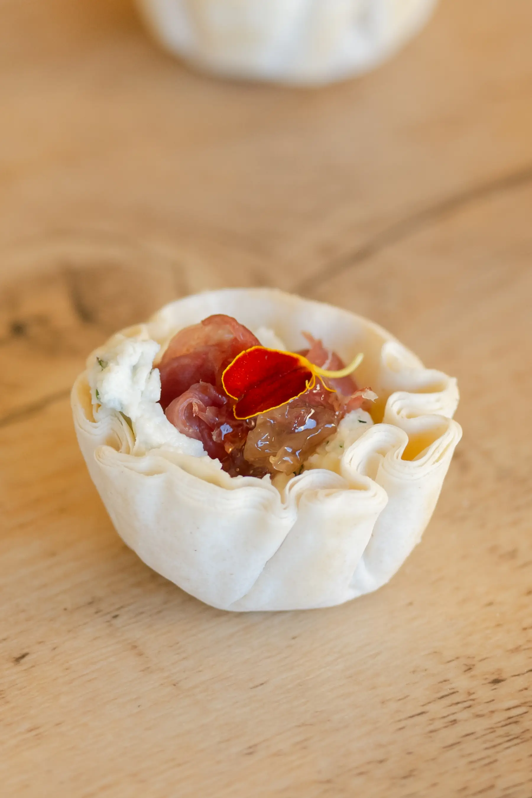 A phyllo cup of goat cheese and prosciutto with rose preserve, topped with a rose petal
