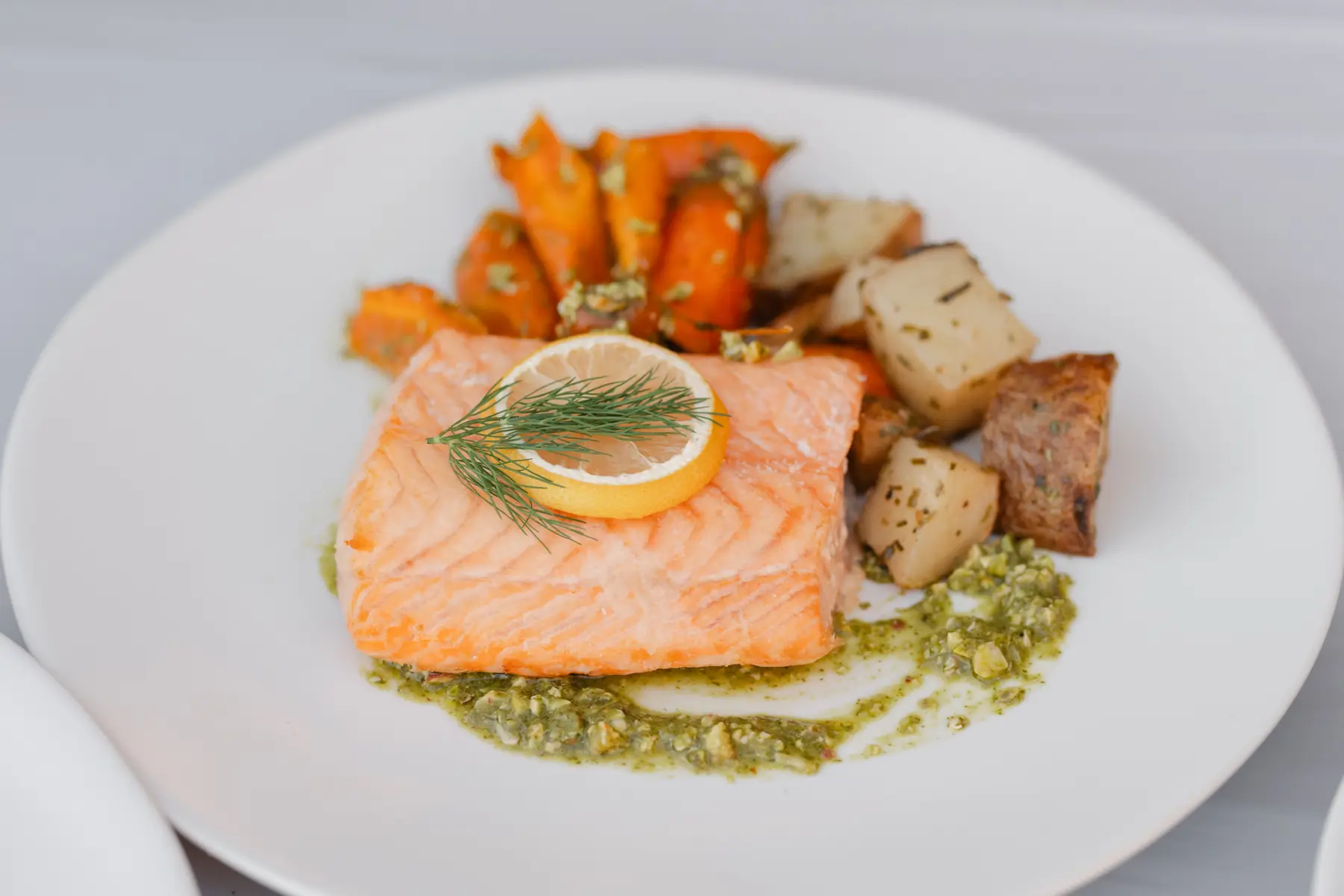A salmon fillet with dill and roasted lemon, Greek lemon potatoes and roasted carrots with pistachio mint pistou