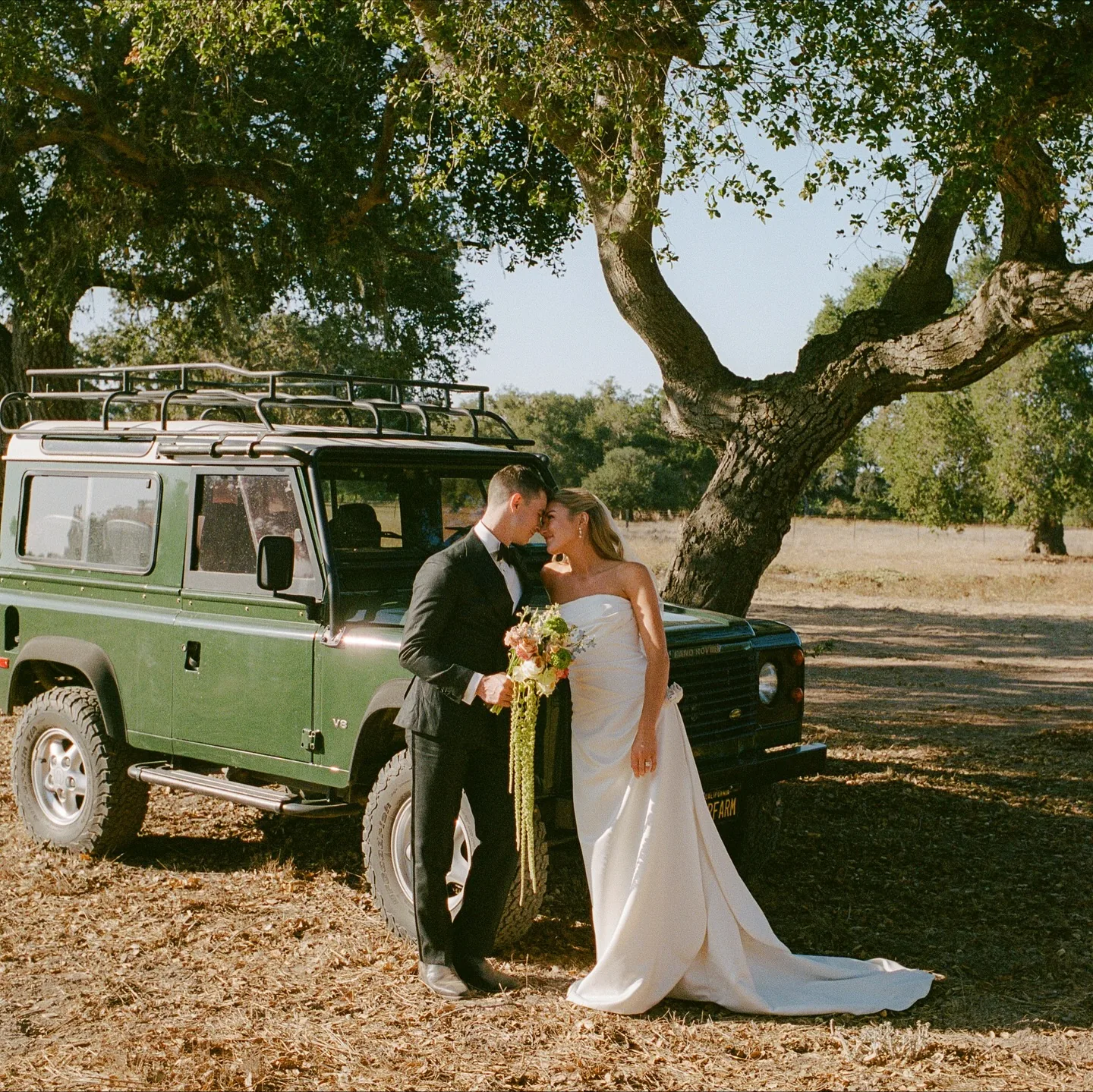 Newlyweds by a vintage Land Rover under a valley oak