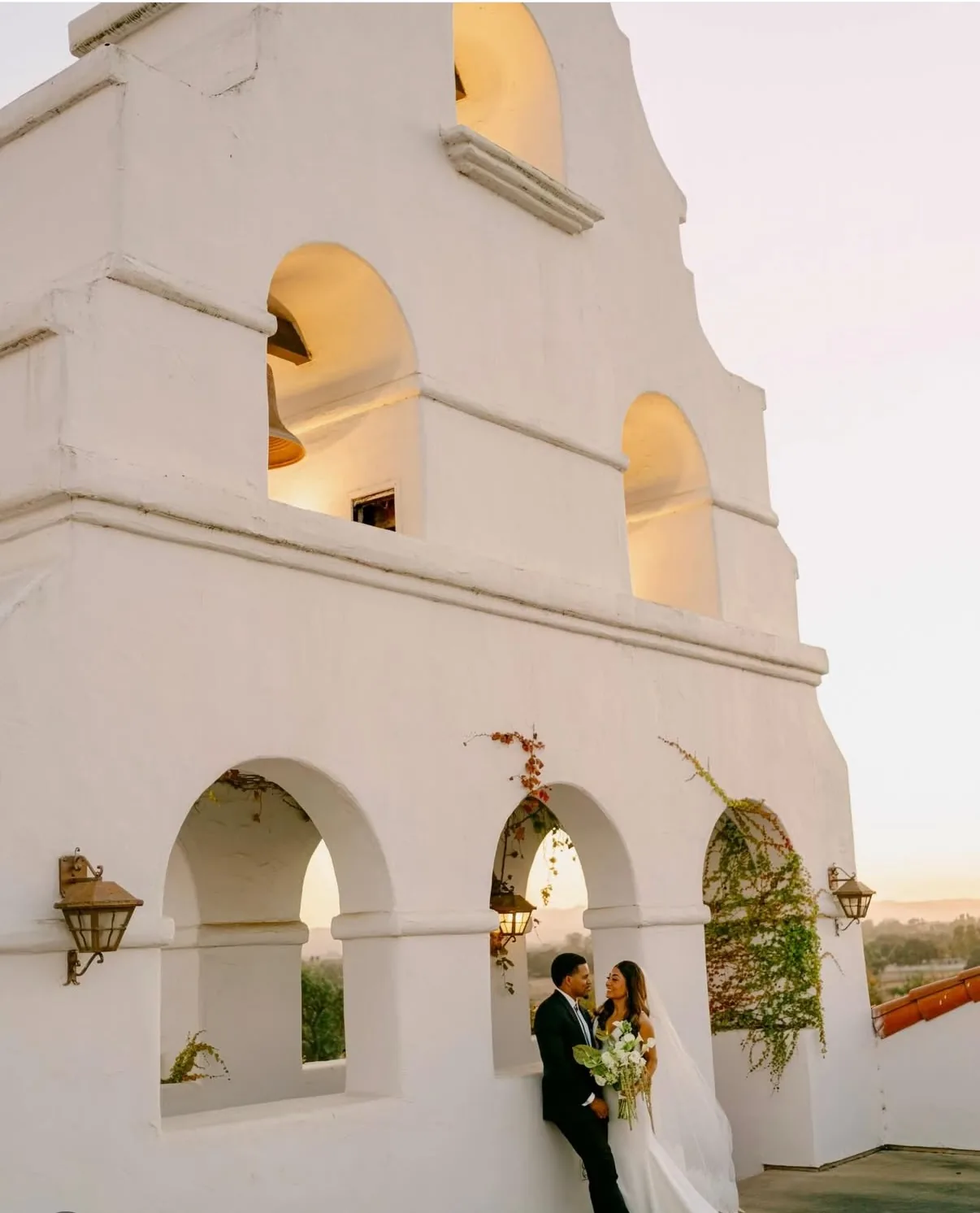 The mission bell tower glowing at sunset at Santa Ynez Ranch, a couple beneath the arcade