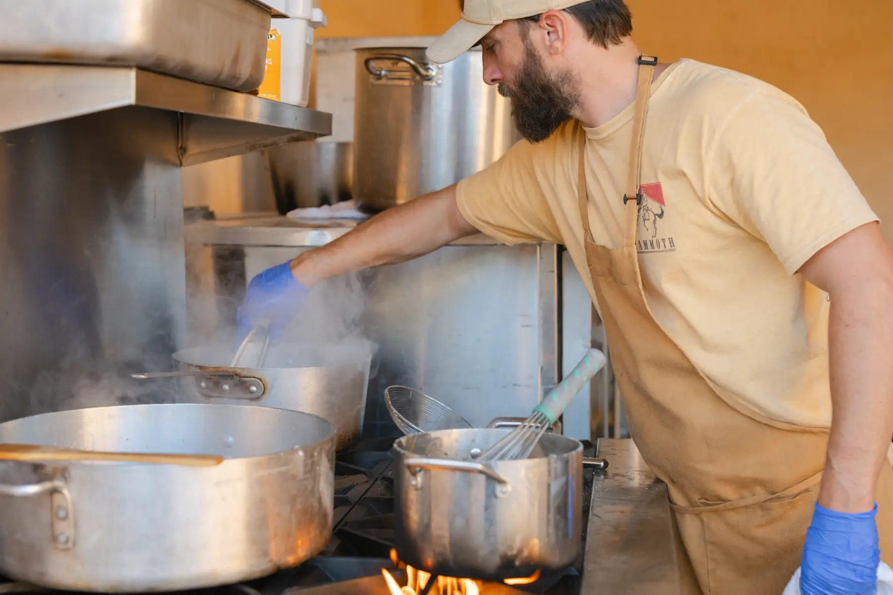 A chef tending stockpots over open flame in a field kitchen