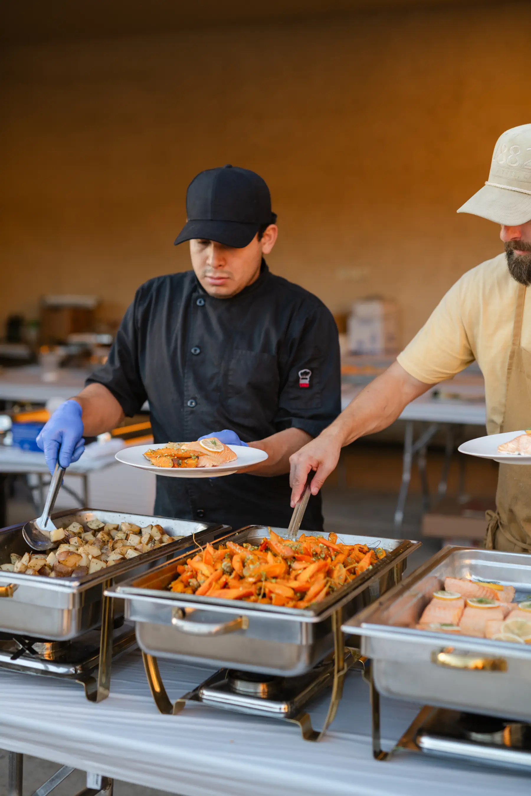 Two chefs plating salmon with roasted potatoes and carrots from the chafing dishes at Sunstone Villa