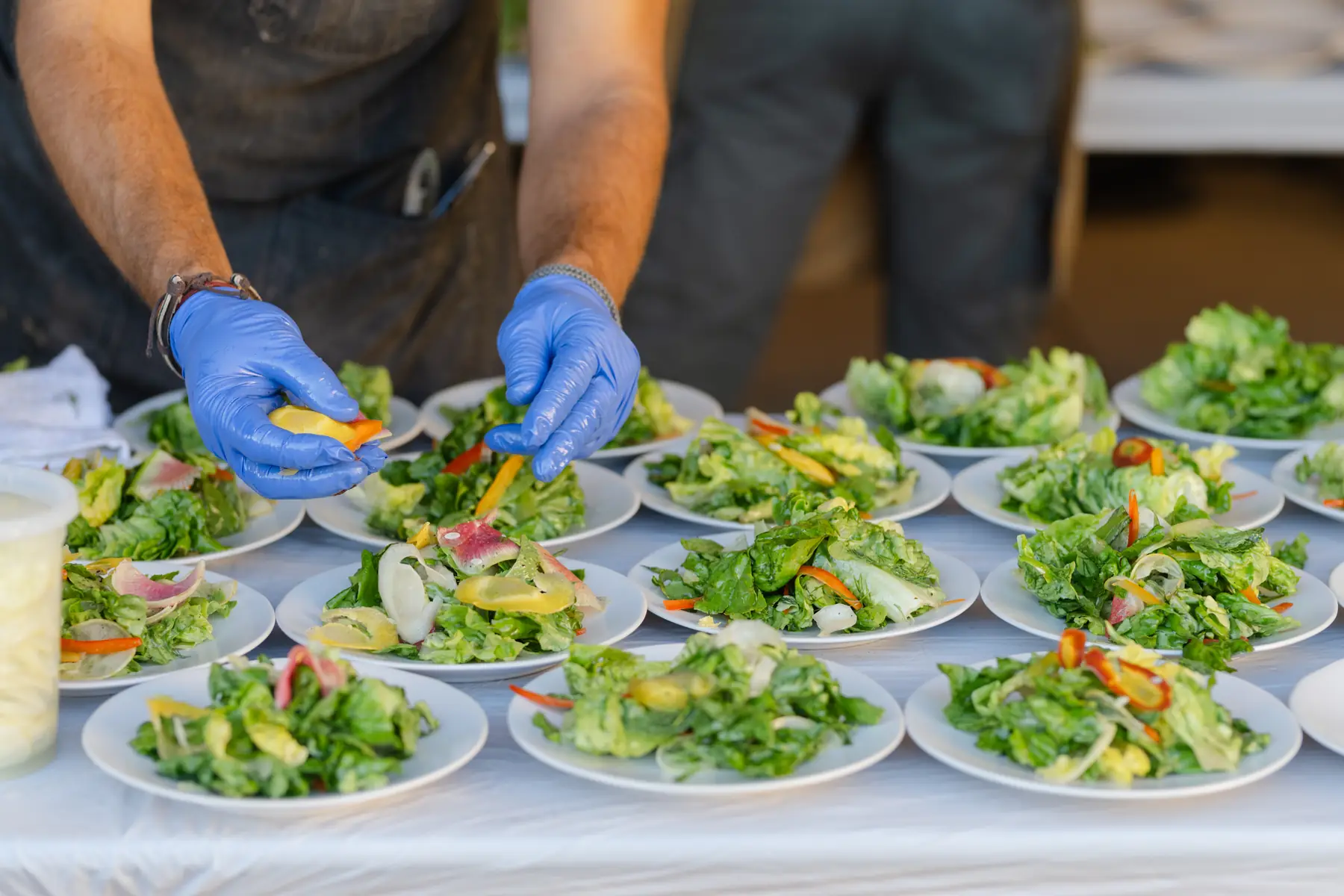 Gloved hands finishing rows of plated salads along the service line
