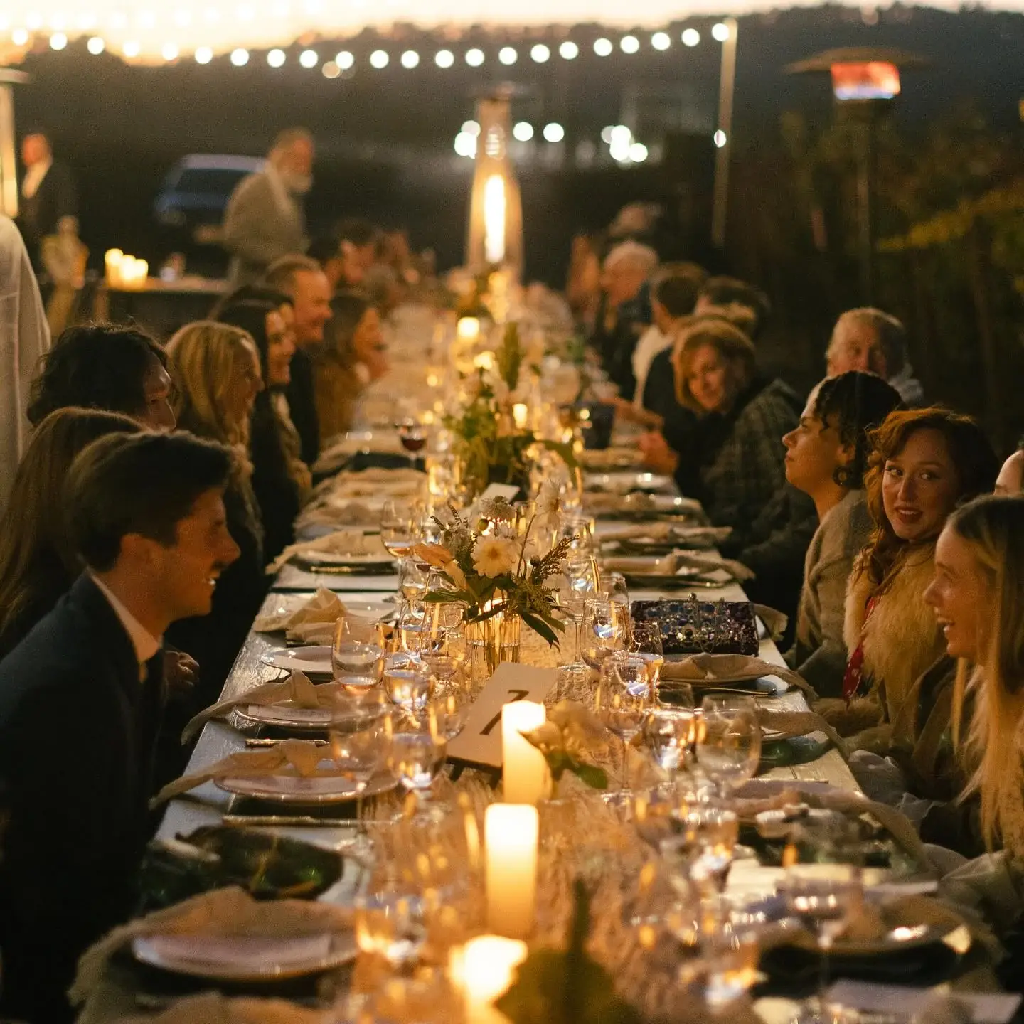 Guests seated along one long candlelit table under string lights at Stolo Vineyards
