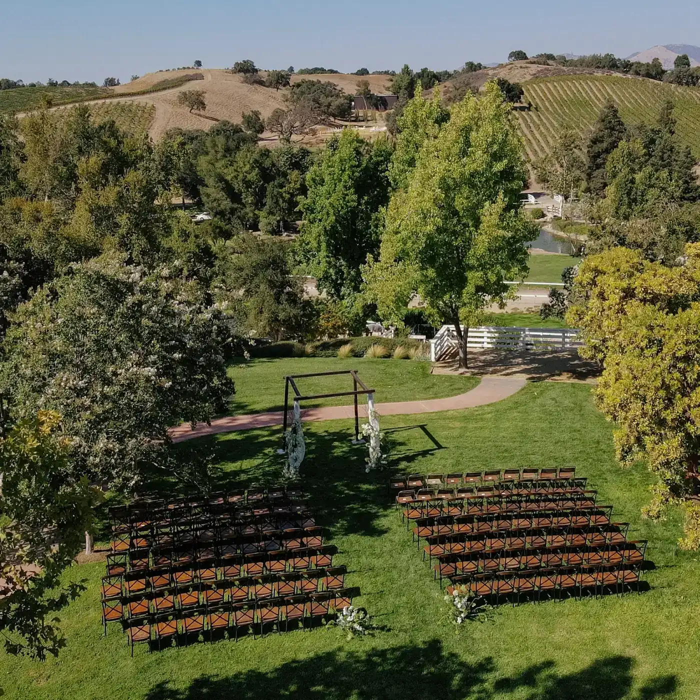 Two blocks of wooden chairs and a draped arbor on the lawn at Santa Ynez Ranch, from above