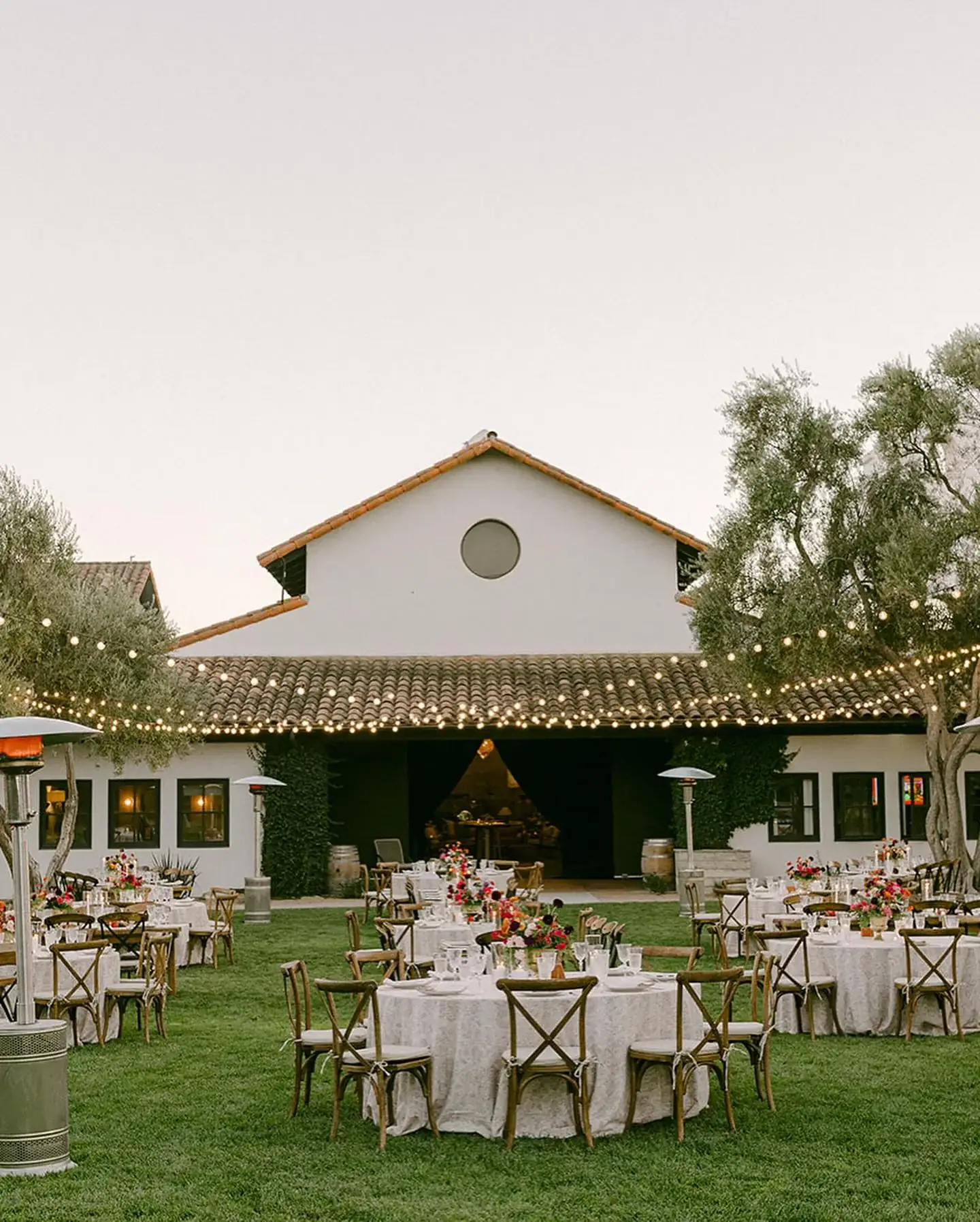 Round tables under string lights on the lawn at dusk at Santa Ynez Ranch