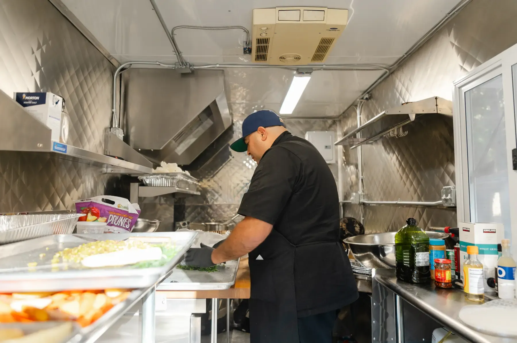 Inside the mobile kitchen we bring to Zaca Lake — a chef plating along the stainless line under the hood