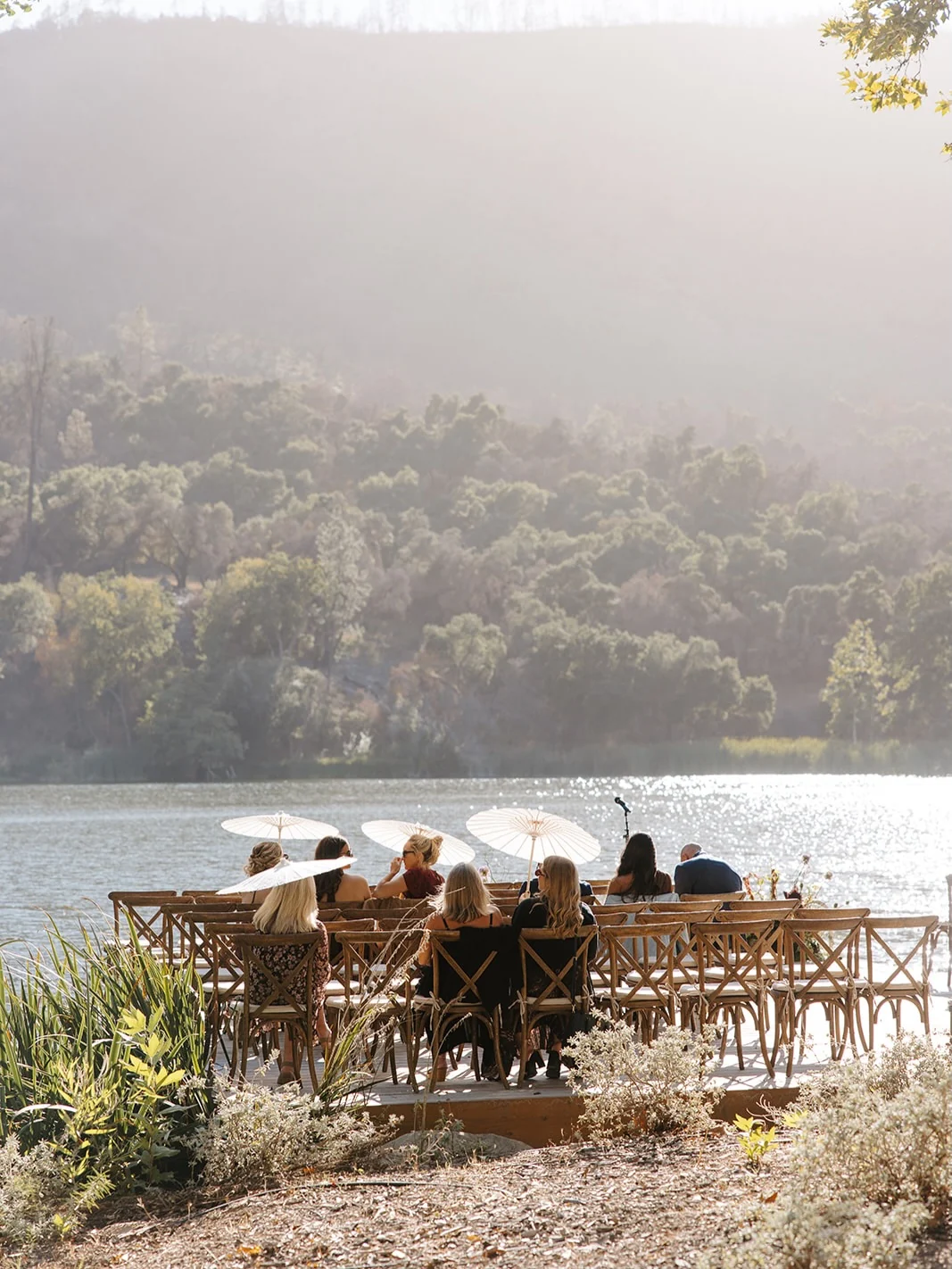 Guests seated under paper parasols in wooden chairs at the water’s edge at Zaca Lake