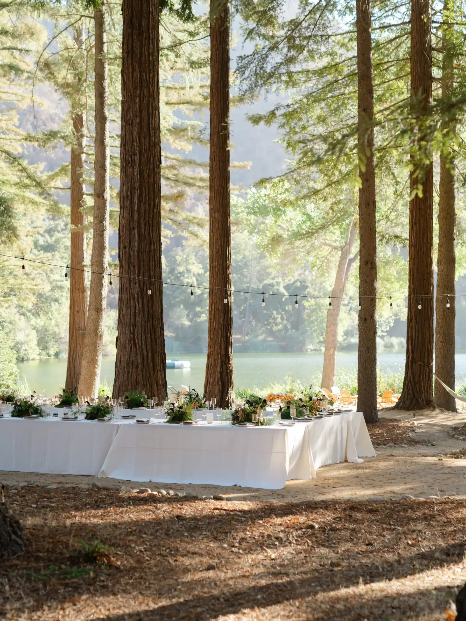 Long white-linen tables set among the redwoods with the lake beyond at Zaca Lake