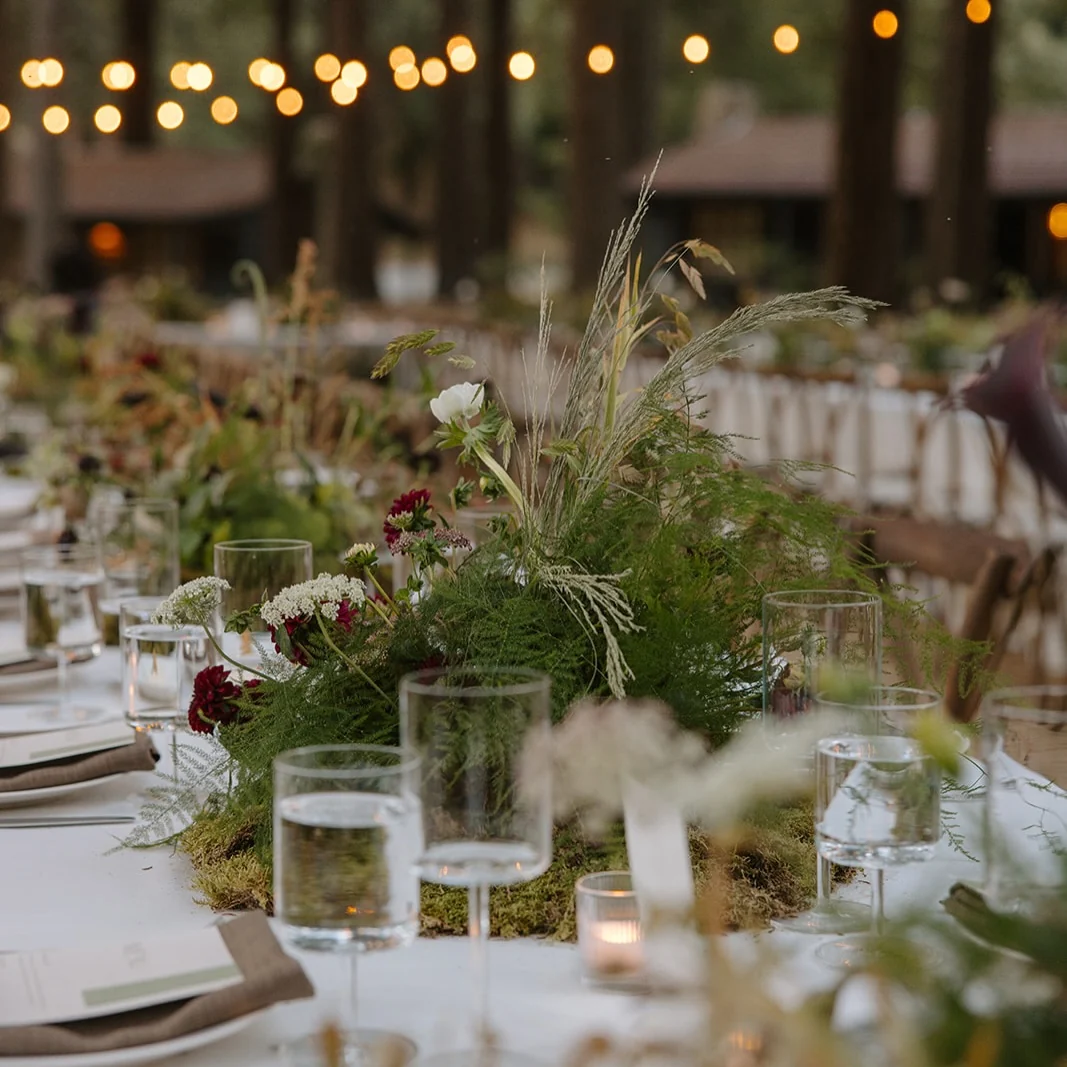 Wild grasses, dark blooms and glassware down a candlelit table at Zaca Lake